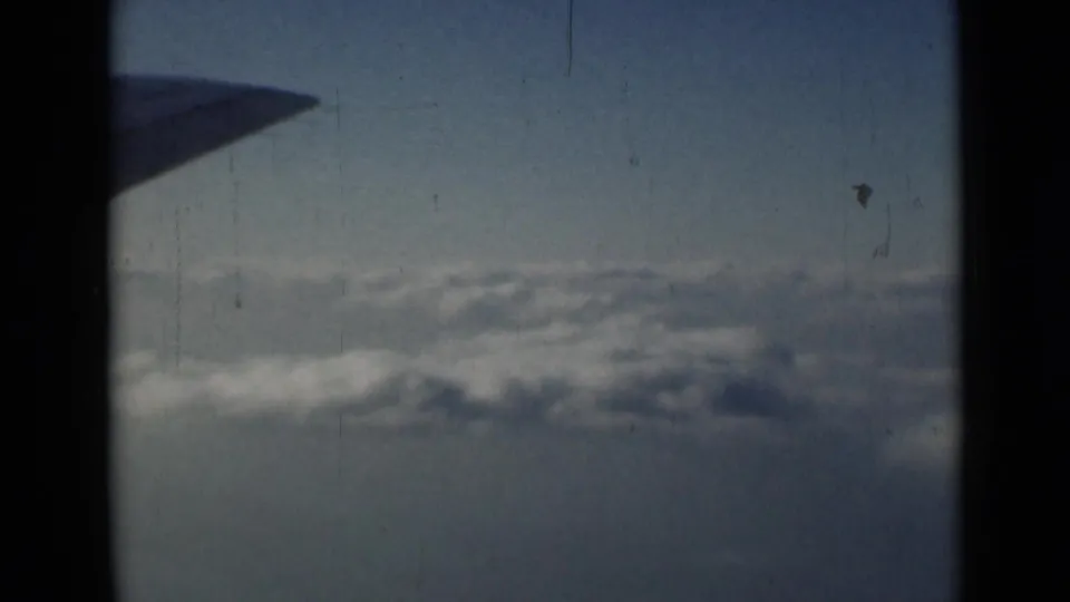 Window-seat view from 1946 8mm footage, with the aircraft wing tip at upper left and a textured cloud layer below.