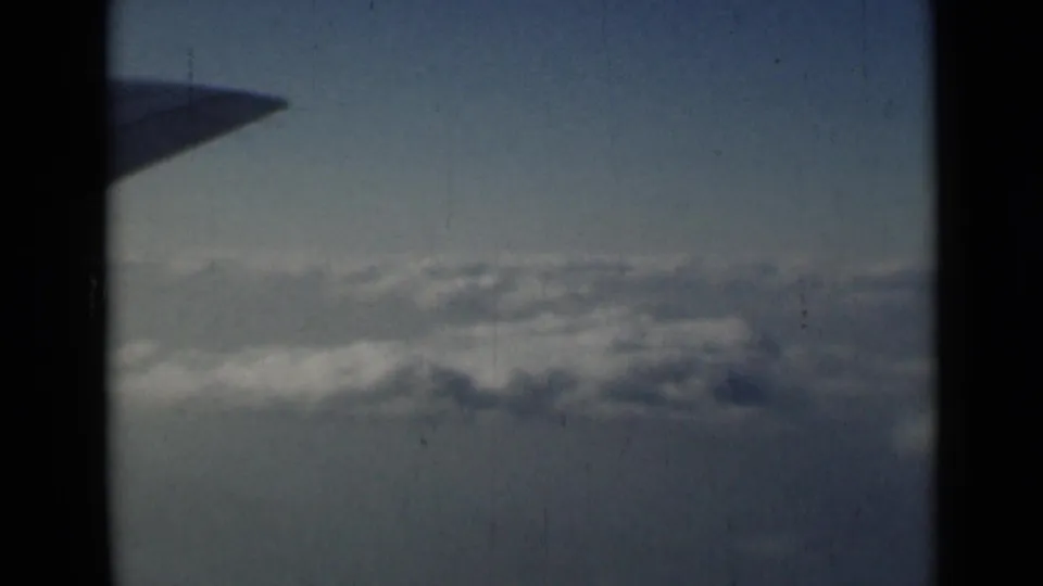 Archival 8mm frame of an airplane wing over gray-white clouds, with visible grain and fading consistent with the supplied 1946 metadata.