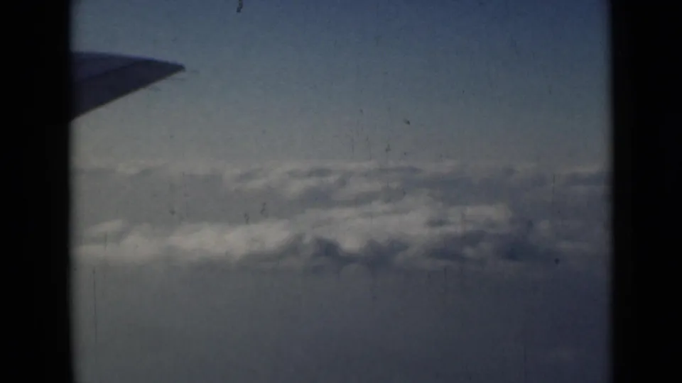 End frame from the 1946 airplane-window clip, showing the wing over soft blue-gray sky and clouds with visible 8mm wear.
