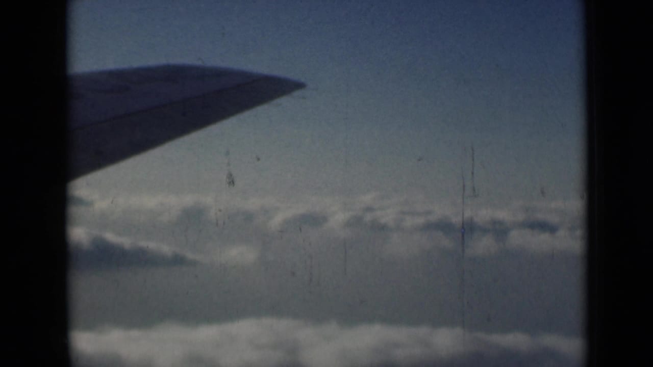 1946 8mm frame with a plane wing near the upper left, clouds below, and vertical film wear visible.