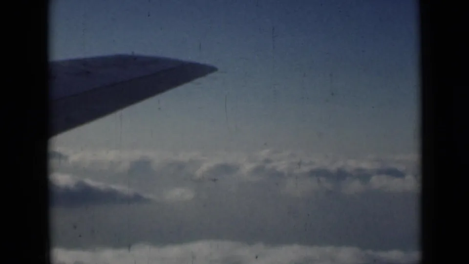 1946 8mm frame showing a dark wing shape over a broad cloud layer, with grain and gate edge visible.