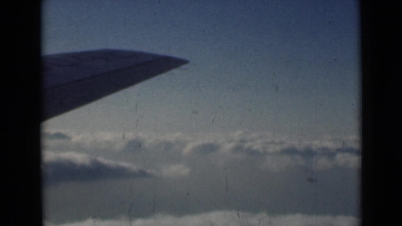 1946 home-movie frame of an airplane wing above a cloud layer, viewed through dark window or film-gate framing.