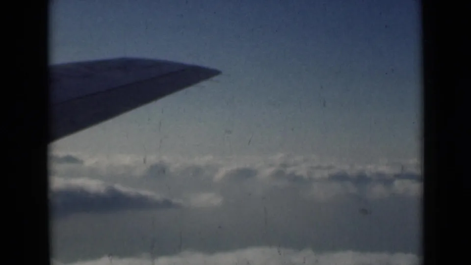 1946 home-movie frame of an airplane wing above a cloud layer, viewed through dark window or film-gate framing.
