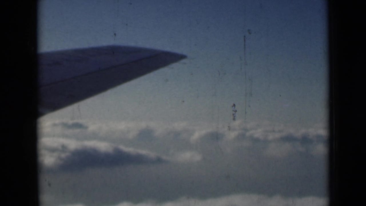 Airplane wing above clouds with heavy dark frame edges.