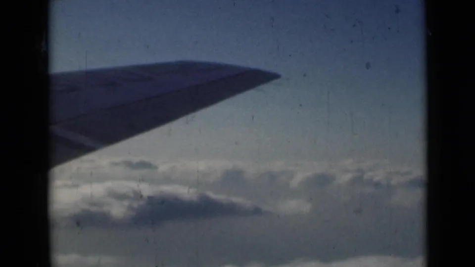 1946 home-movie view of an aircraft wing over a thick cloud layer, softened by grain, fading, and scratches.