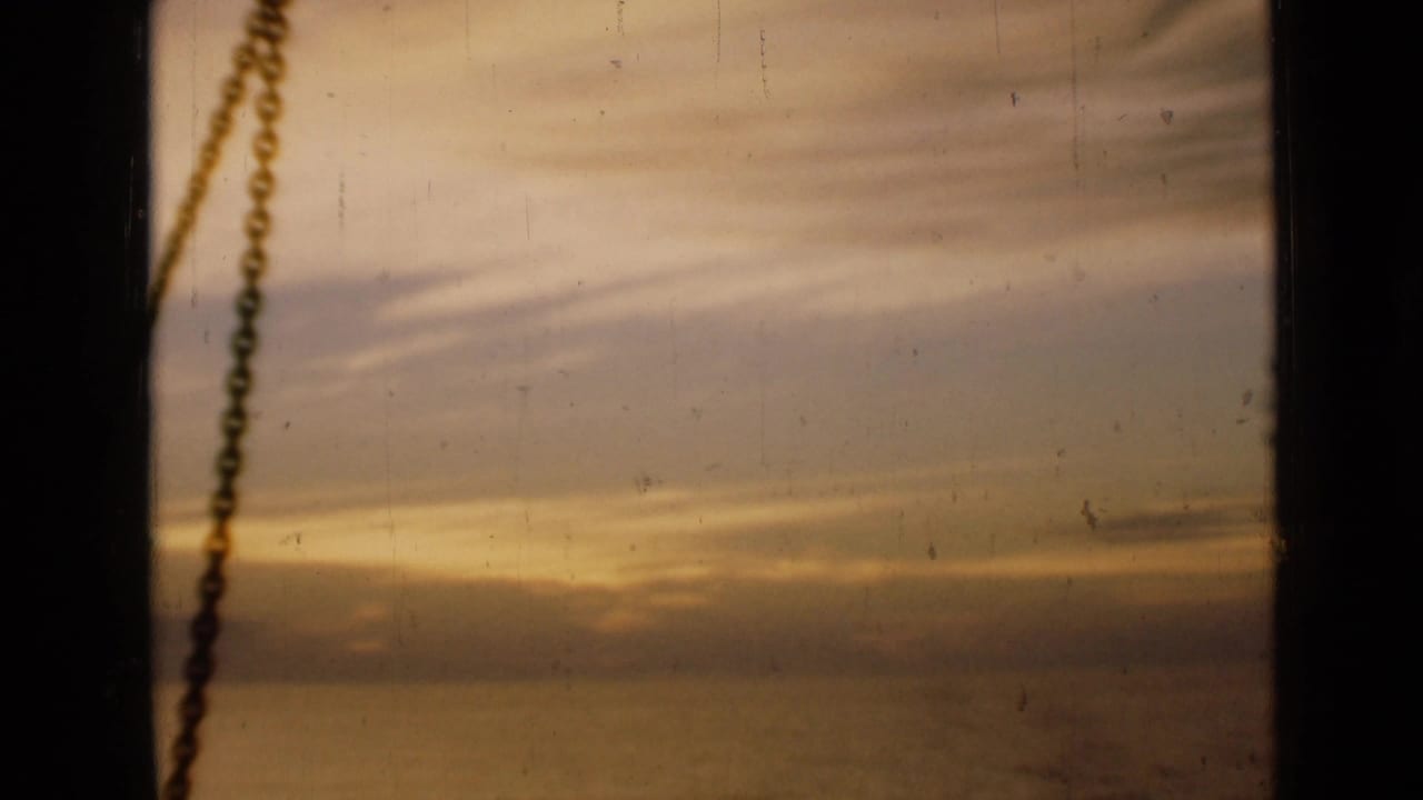 1946 London 8mm frame showing a golden sunset and cloud band through a window, with a chain hanging near the left side.