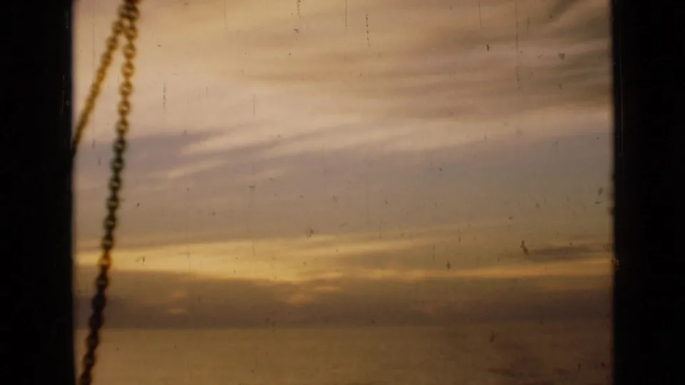 1946 London 8mm frame showing a golden sunset and cloud band through a window, with a chain hanging near the left side.