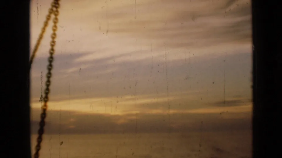 1946 London home-movie still of a softly exposed sunset through a window, marked by a hanging chain and visible 8mm wear.
