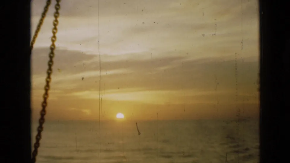 The 1946 8mm frame shows a low sun over water under pale cloud layers, with the window chain partly visible at the left edge.
