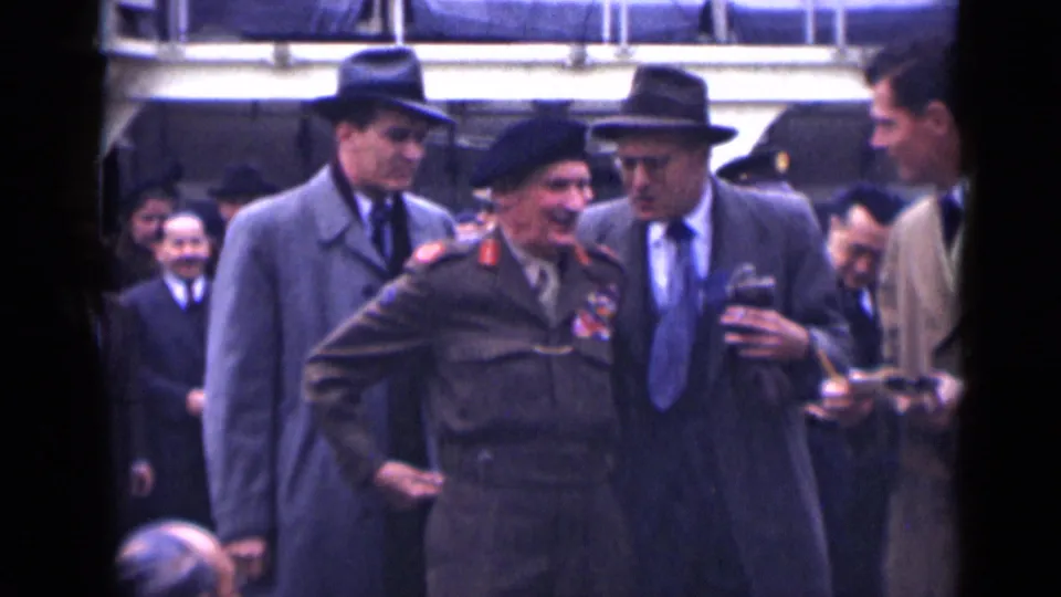 In 1946 London footage, a decorated army officer in beret and uniform walks with suited men and onlookers outside a formal building.