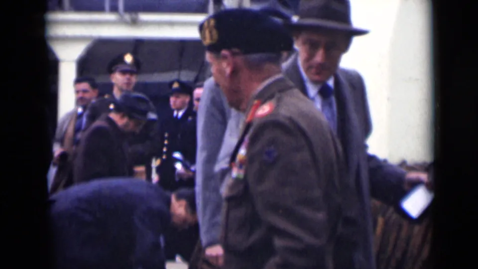 A side view shows the decorated army officer turning among suited men, uniformed personnel, and onlookers in the 1946 London scene.