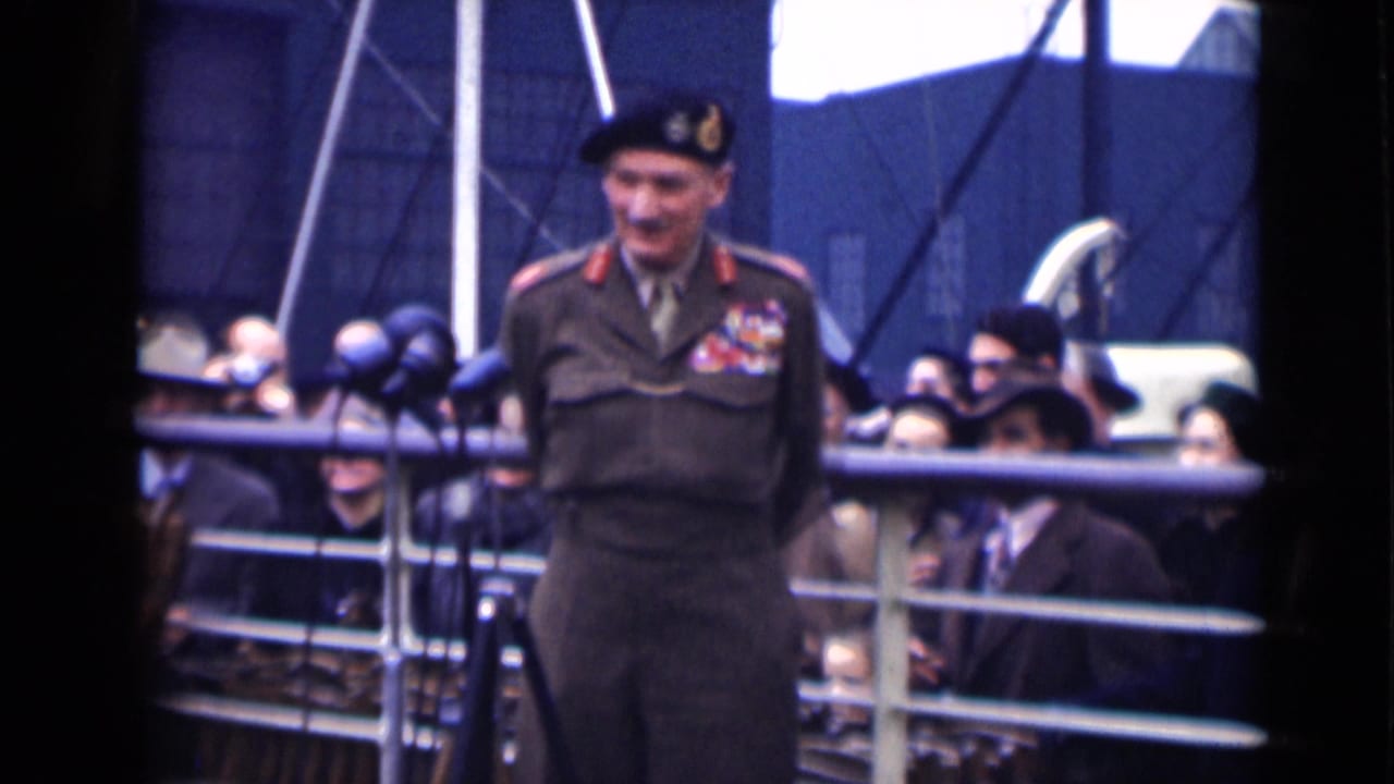 A uniformed officer in 1946 London appears to smile while addressing a crowd from a microphone position at a public event.