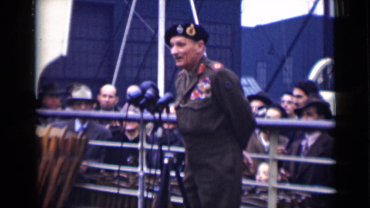 In London 1946 home-movie footage, a decorated uniformed officer stands on a ship deck near microphones as civilians watch behind railings.