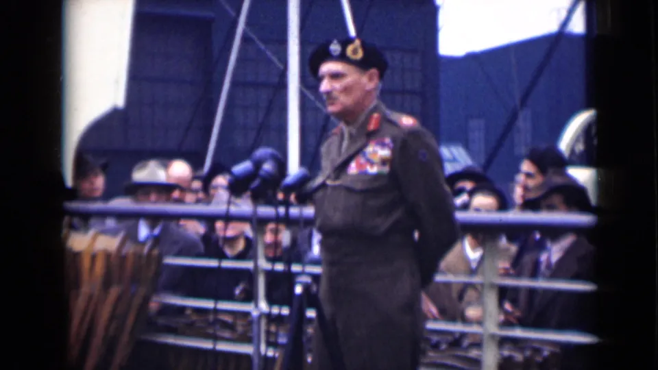 At the end of the clip, the decorated officer stands near microphones with his hands behind his back as the crowd remains gathered behind him.