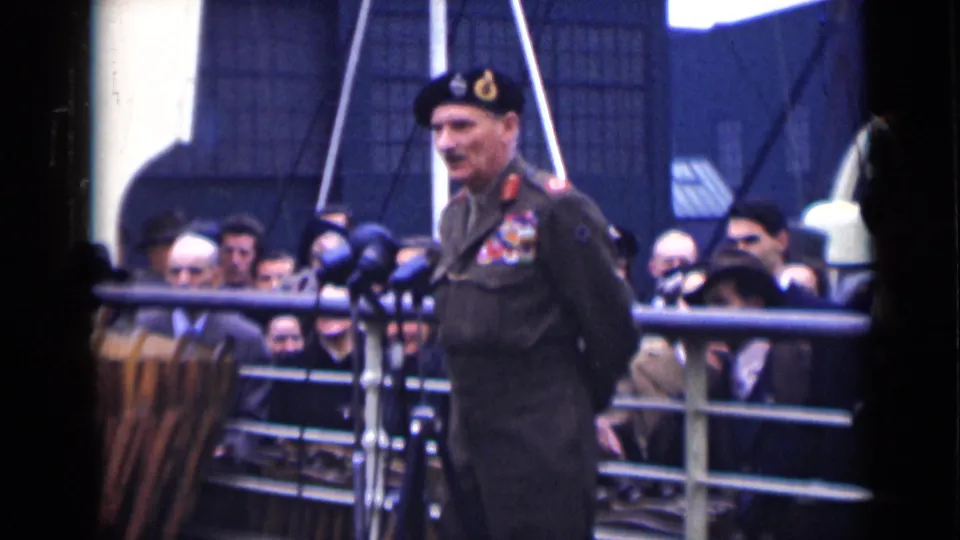 Final frame shows the uniformed speaker turned slightly at the microphones, with a compact civilian audience behind him in London 1946 footage.