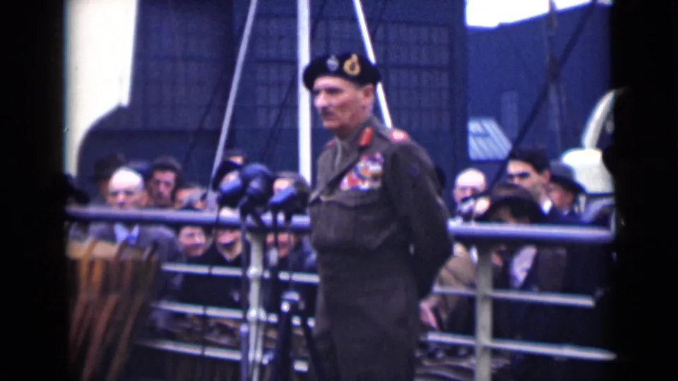 In 1946 London footage, a decorated military officer in a beret stands at microphones with civilians gathered behind railings.