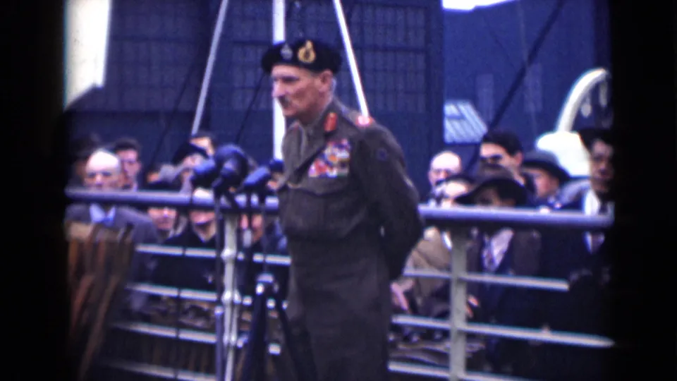 A decorated military officer in beret and dark uniform stands at microphones during an outdoor London public gathering in 1946.