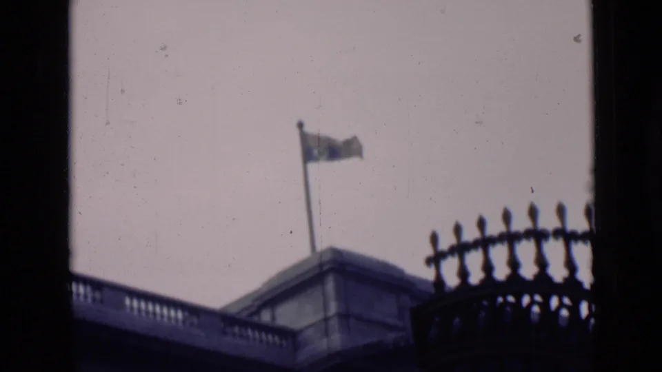 The final frame holds on the flagpole, stone roofline, and silhouetted ironwork against a pale sky.
