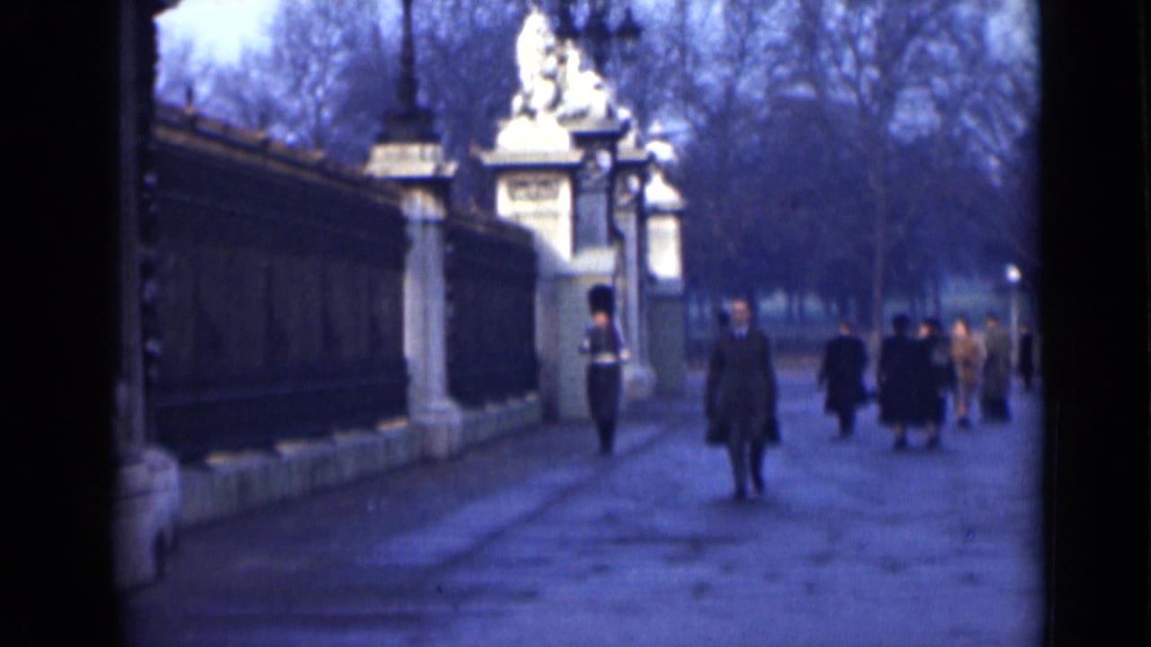 1946 London home-movie frame showing a paved path, ornate gate, uniformed guard, and pedestrians in overcoats.