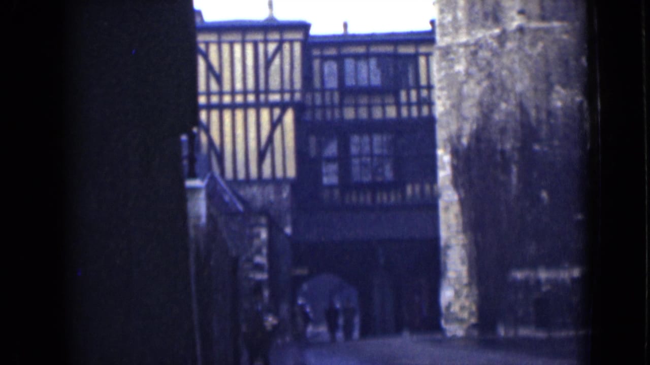 1946 London home-movie frame showing a half-timbered building and arched passage beyond dark foreground walls.