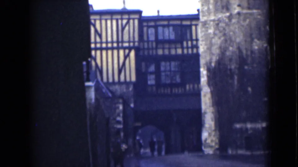 1946 London home-movie frame showing a half-timbered building and arched passage beyond dark foreground walls.