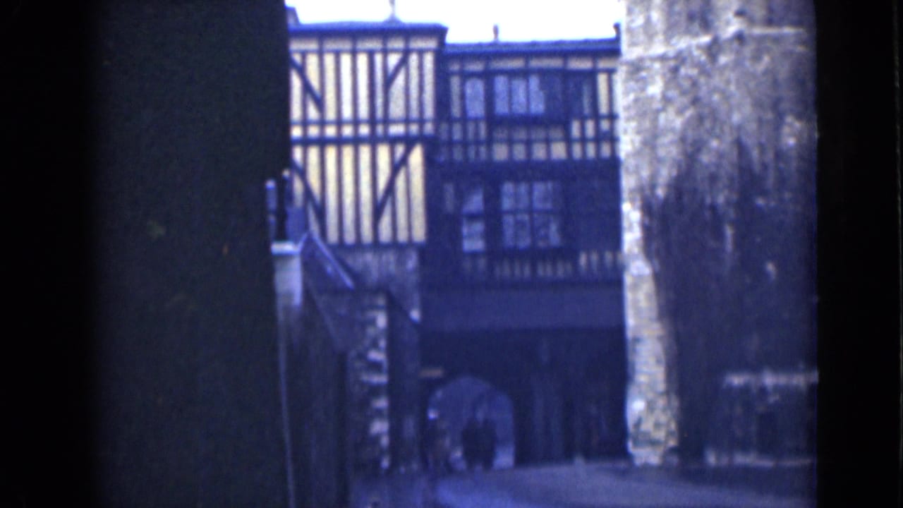 London 1946 home-movie frame showing a timber-framed historic building viewed through a shadowed archway and stone wall.