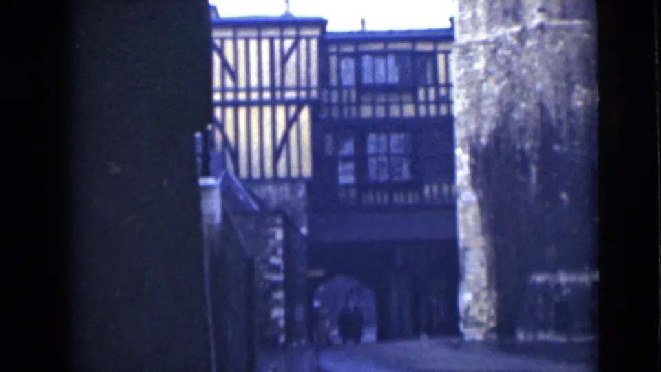 London 1946 home-movie frame showing a timber-framed historic building viewed through a shadowed archway and stone wall.