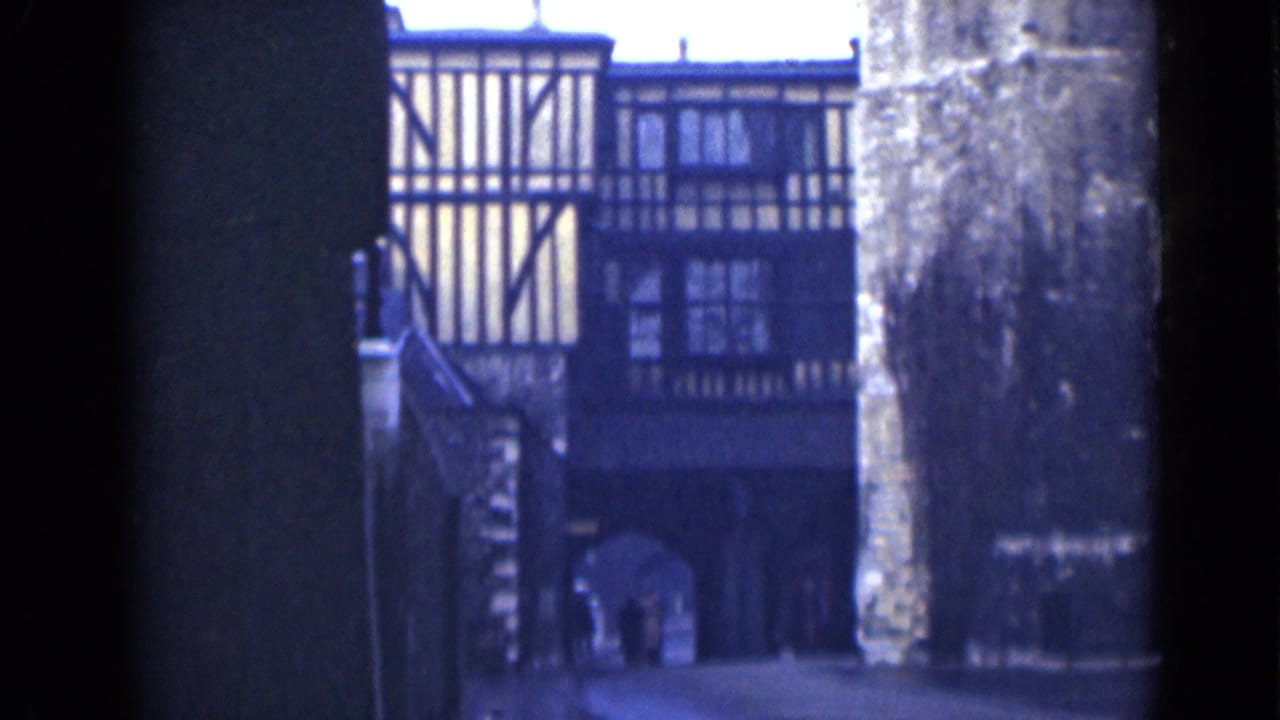 Similar view of a timber-framed facade beyond a dark passage and stone wall.