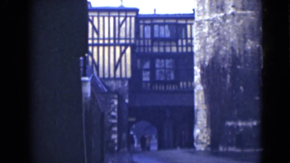 London 1946 frame with a soft 8mm view of timber-framed architecture beyond a shaded archway and stone masonry.