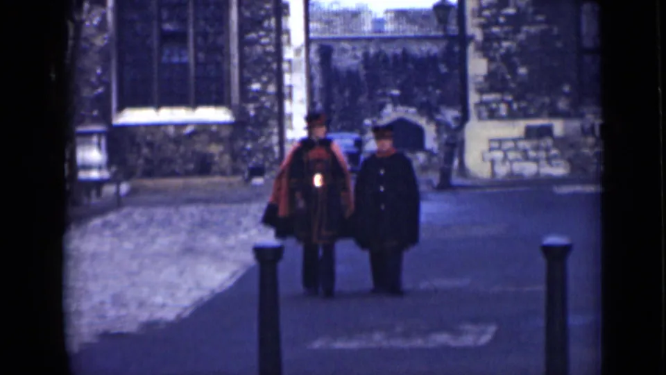The two men draw nearer in the 1946 London courtyard, showing the red ceremonial garment, dark coat, hats, and paved path more clearly.