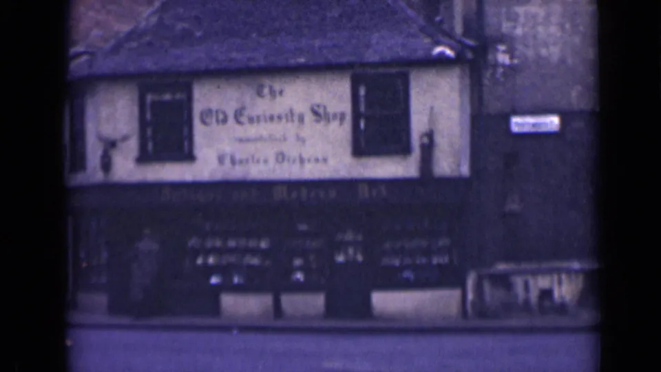 1946 London view of The Old Curiosity Shop exterior with painted upper sign, dark ground-floor shopfront, display windows, and empty street.