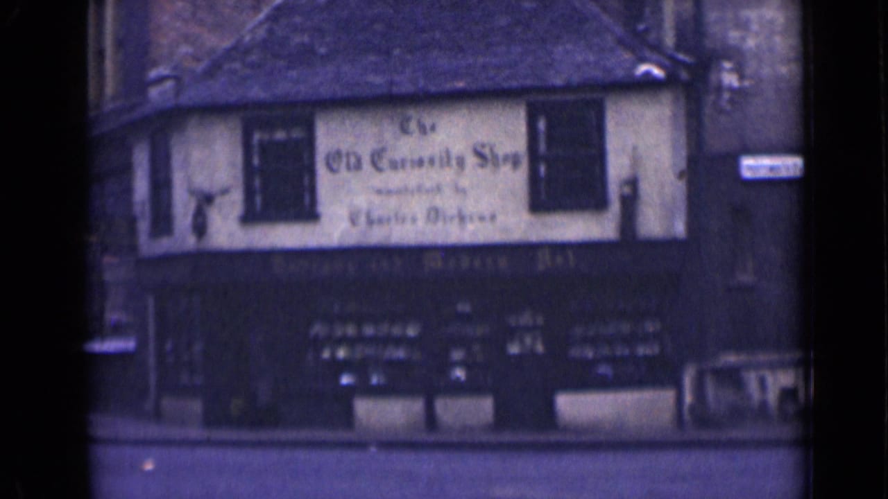 1946 London home-movie frame showing The Old Curiosity Shop across the street, including its upper sign, roofline, windows, and dark shopfront.