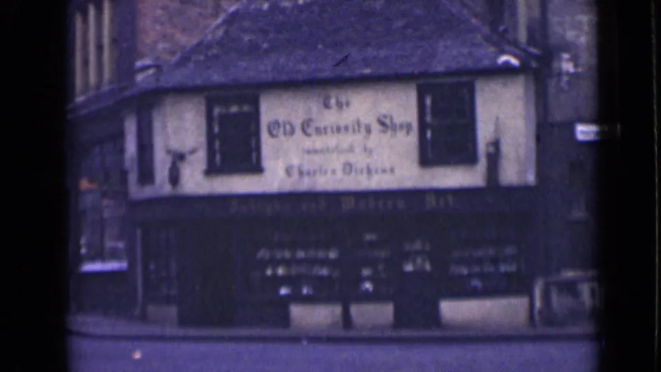 1946 London frame of The Old Curiosity Shop facade, with painted lettering, dark lower storefront, display windows, pavement, and neighboring wall edge.