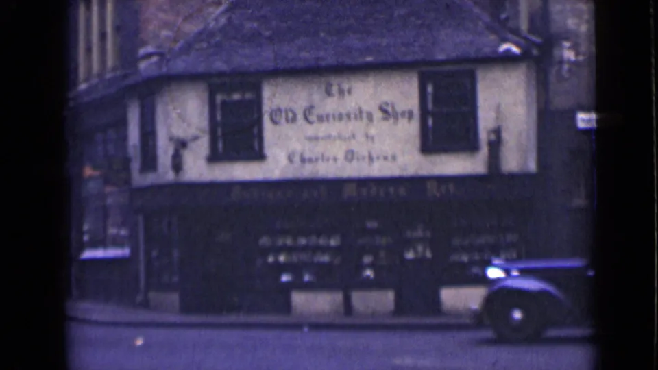 1946 London view of The Old Curiosity Shop with a dark classic car passing at the lower right edge of the street.