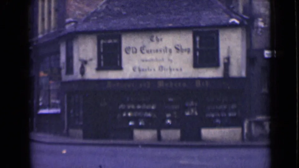 1946 London 8mm frame showing a corner building marked The Old Curiosity Shop, with upper windows and a dark storefront below.