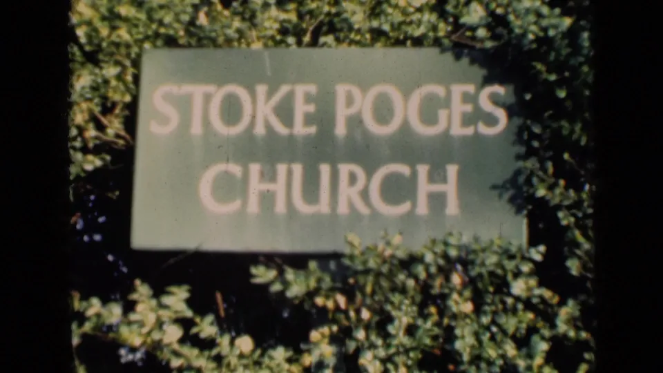 8mm home-movie frame showing the Stoke Poges Church sign in soft focus, bordered by dense greenery and film gate edges.