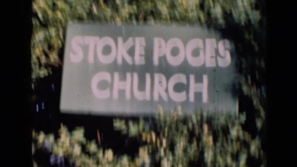 A slightly closer and more blurred view of the Stoke Poges Church sign, with leaves and shadow crossing the frame.