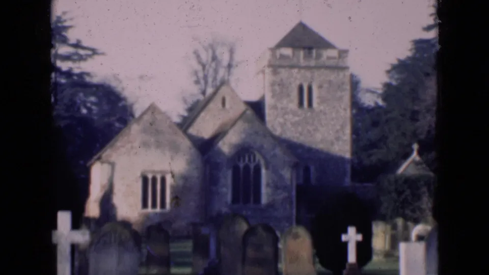 A stone church with arched windows and a square tower stands behind gravestones and crosses in an English churchyard setting.