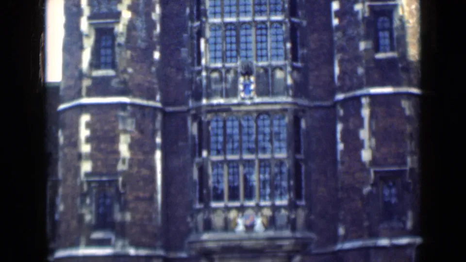 1940s London home-movie frame showing leaded windows, brickwork, and pale stone detailing on a historic building facade.
