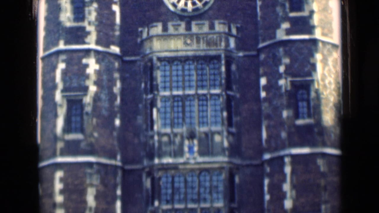 1946 London footage frame showing a Gothic-style facade with a large clock above tall leaded windows and flanking round towers.
