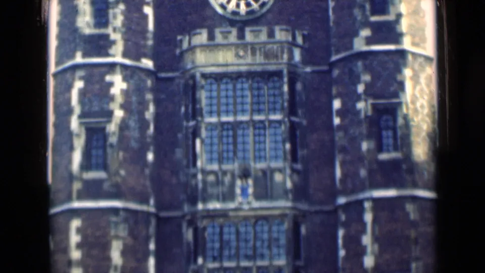 1946 London footage frame showing a Gothic-style facade with a large clock above tall leaded windows and flanking round towers.