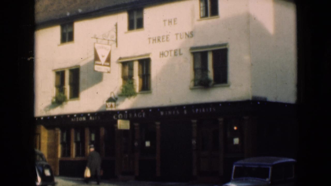 White facade of The Three Tuns Hotel with a man walking past and cars at the street edge.