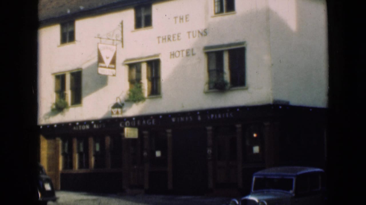 1946 London street frame showing The Three Tuns Hotel facade, pub sign, upper windows and parked vehicles at the curb.