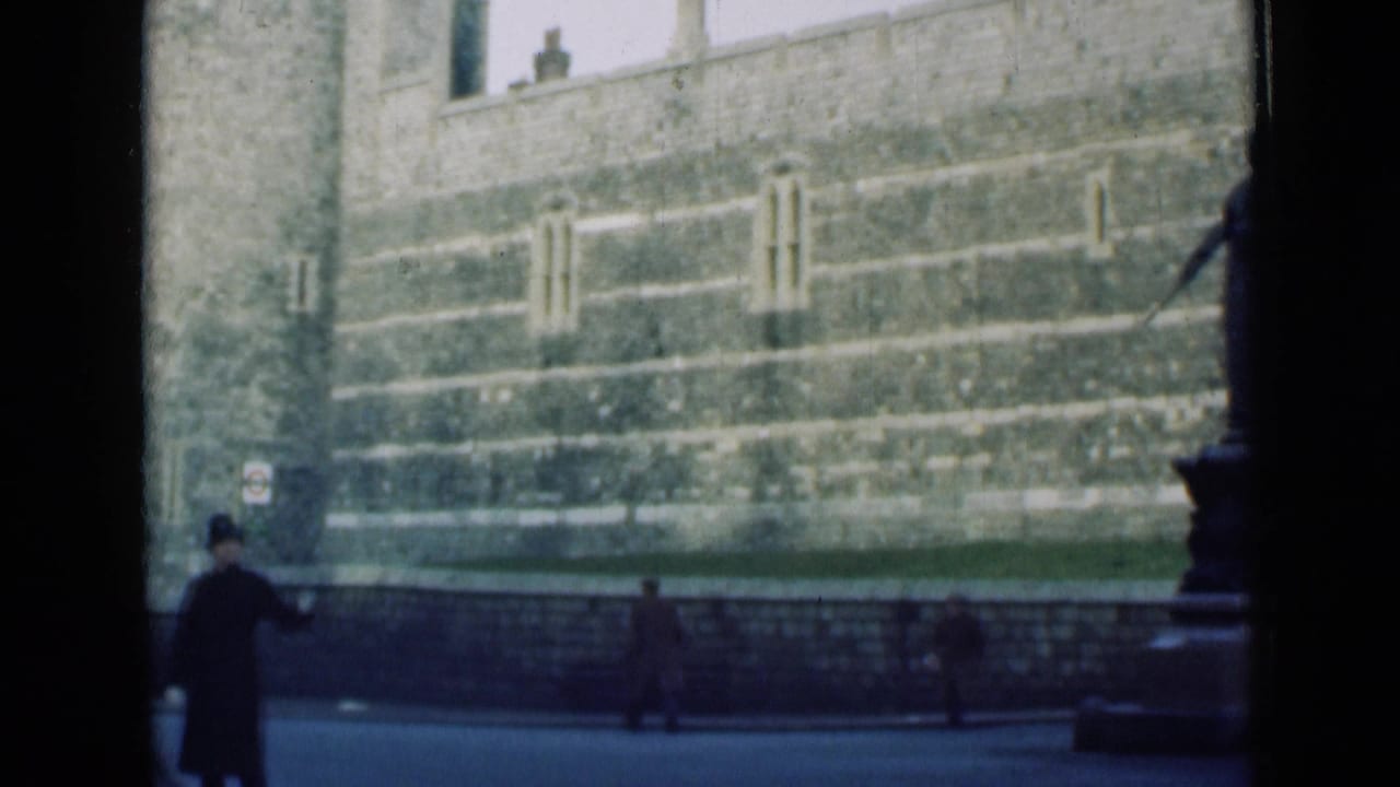 Policeman standing on a London street beside stone landmark walls.