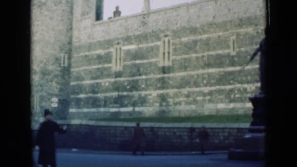 1946 London home-movie frame showing a policeman near railings, pedestrians, and large stone walls across the street.