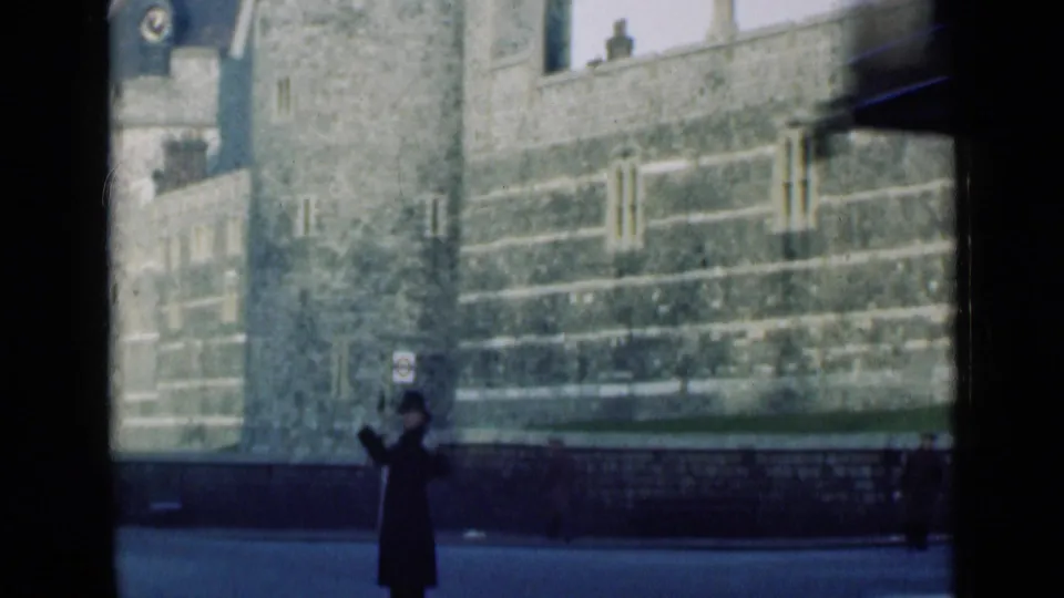 1946 London frame showing a policeman in dark uniform beside railings, with stone walls and a tower visible across the road.