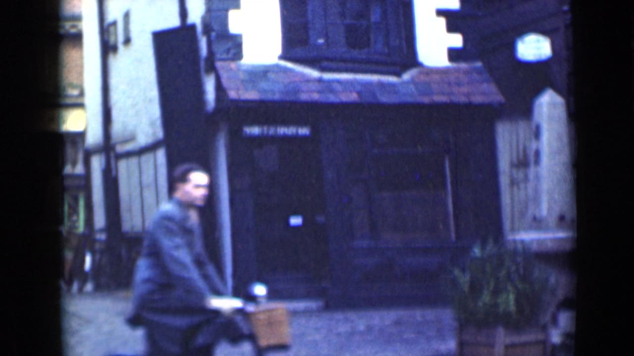 1946 London street frame with a cyclist passing in front of a dark timber-framed building and tiled awning.