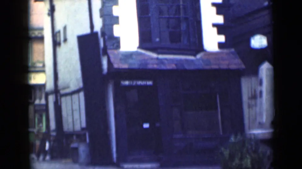 1946 London home-movie frame with a slightly tilted view of the timber-framed building, tiled awning, and cobbled lane.