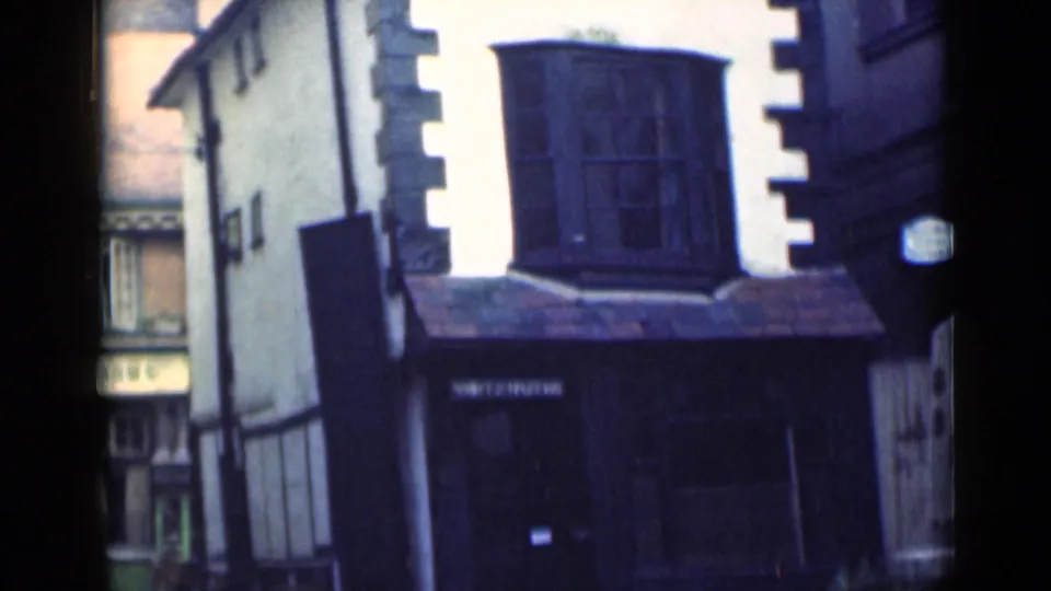 1946 London frame showing the dark timber-framed facade, upper window, tiled awning, and quiet cobbled street edge.