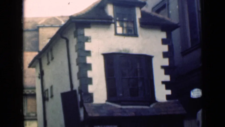 Home-movie frame of a London building corner with stucco walls, dark quoins, and a projecting window bay.